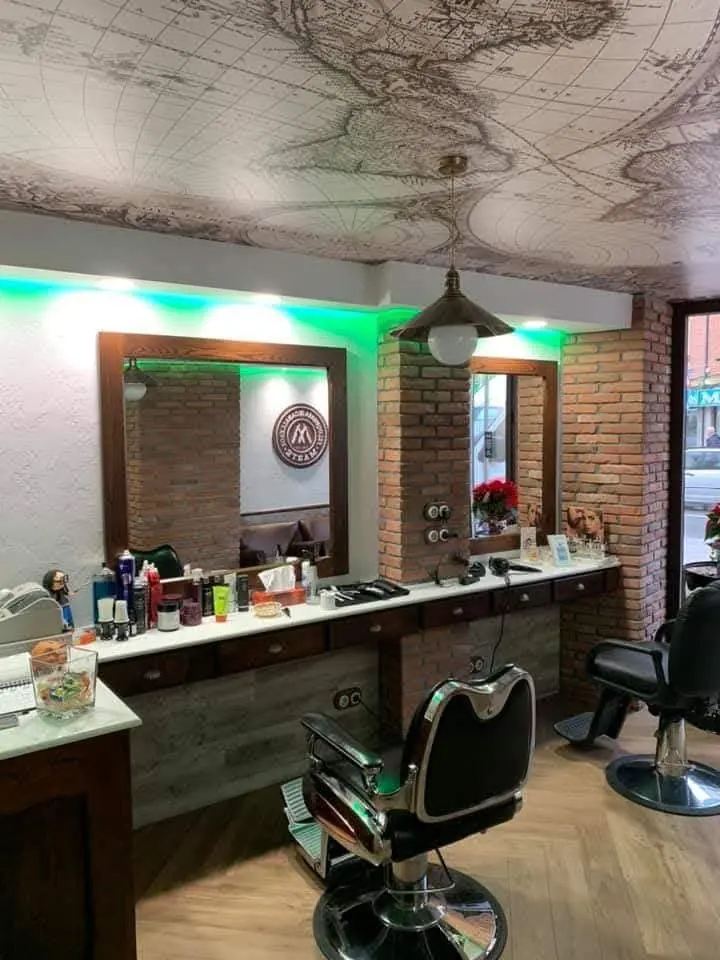 Interior de la peluquería con espejos de marco de madera, pared de ladrillo y sillones de barbero